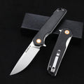 Black folding pocket knife with silver blade and orange pivot accents, shown next to its packaging.