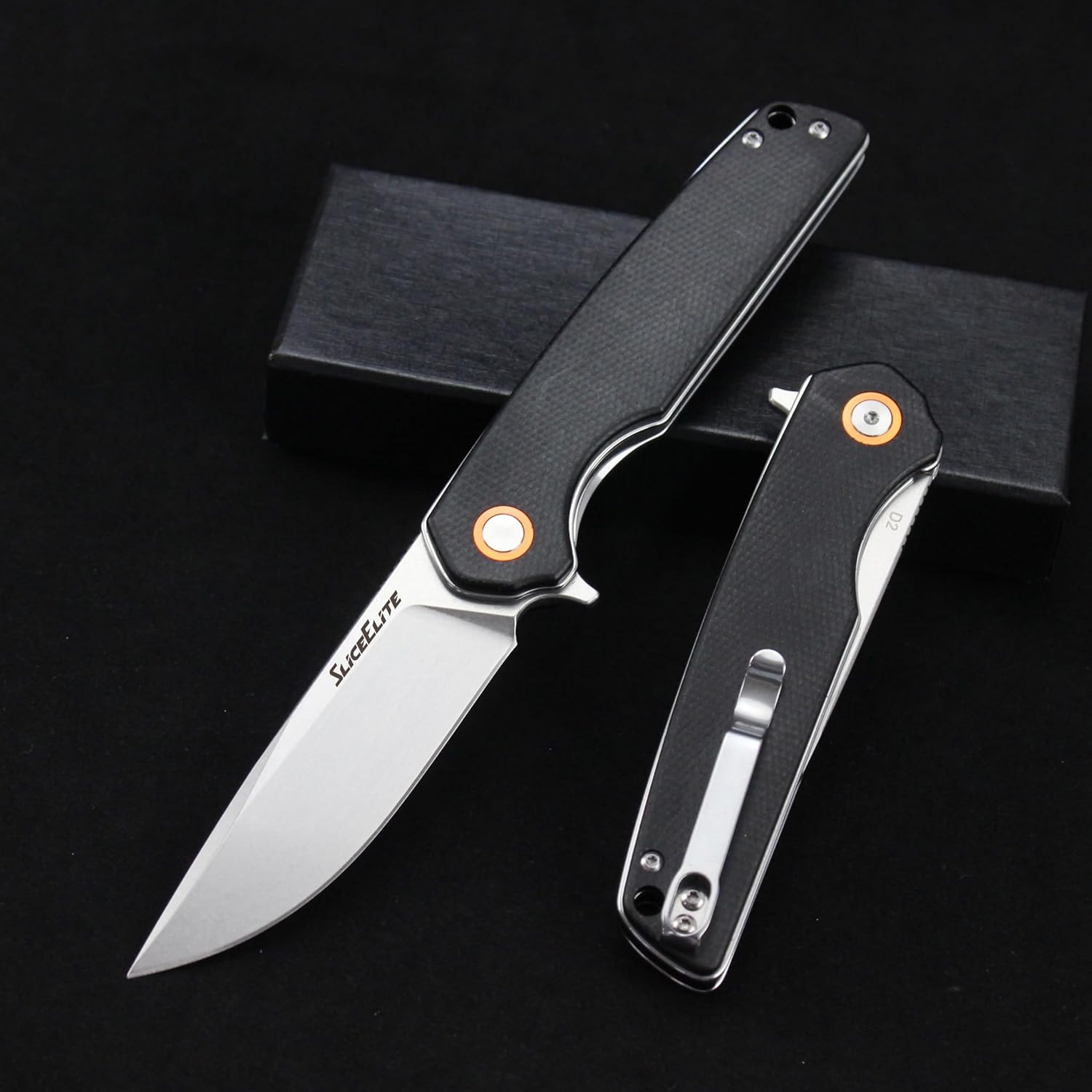 Black folding pocket knife with silver blade and orange pivot accents, shown next to its packaging.